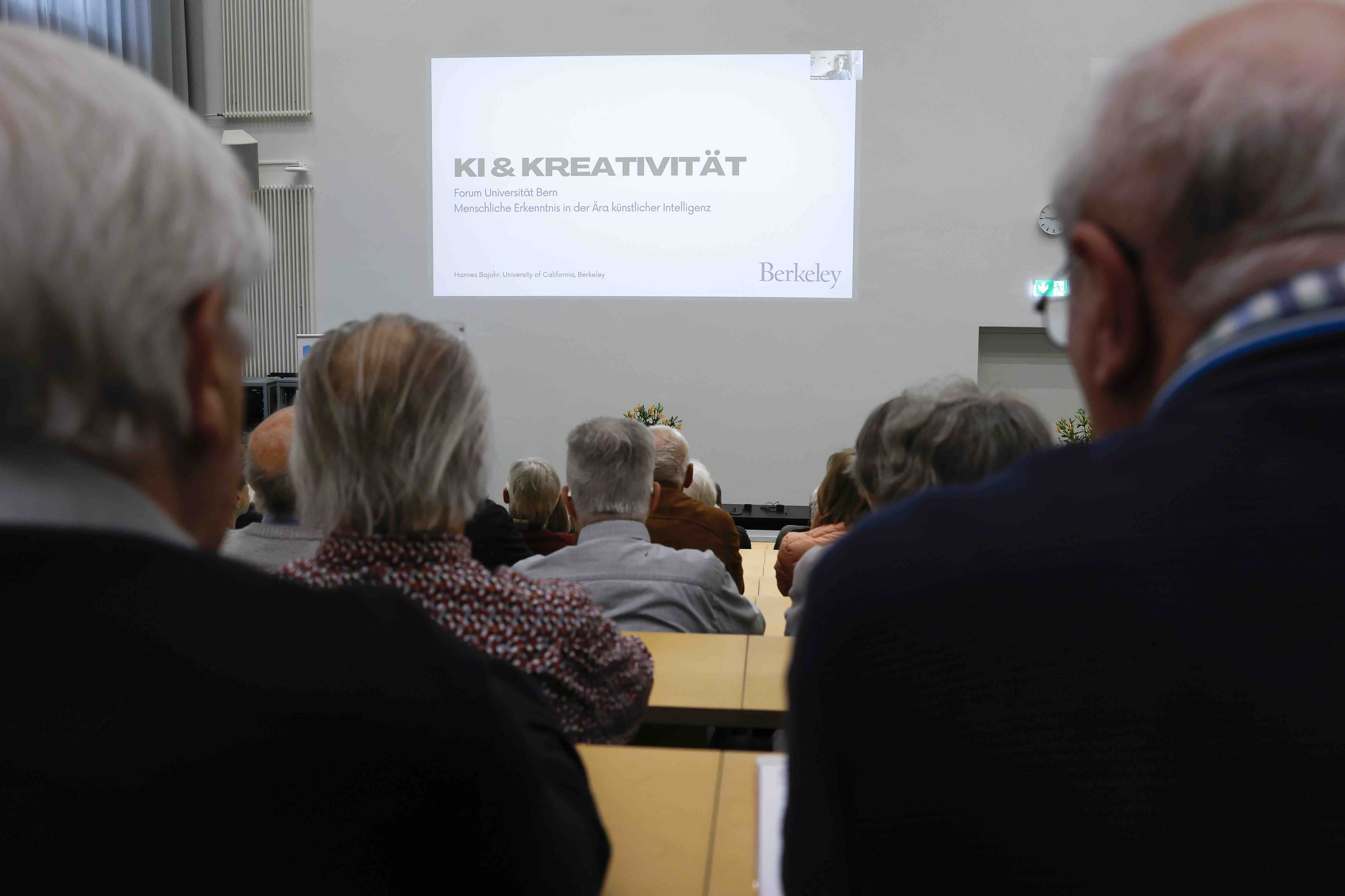 Blick durch die Publikumsreihen im Hörsaal nach vorne zur Projektion einer Präsentation.