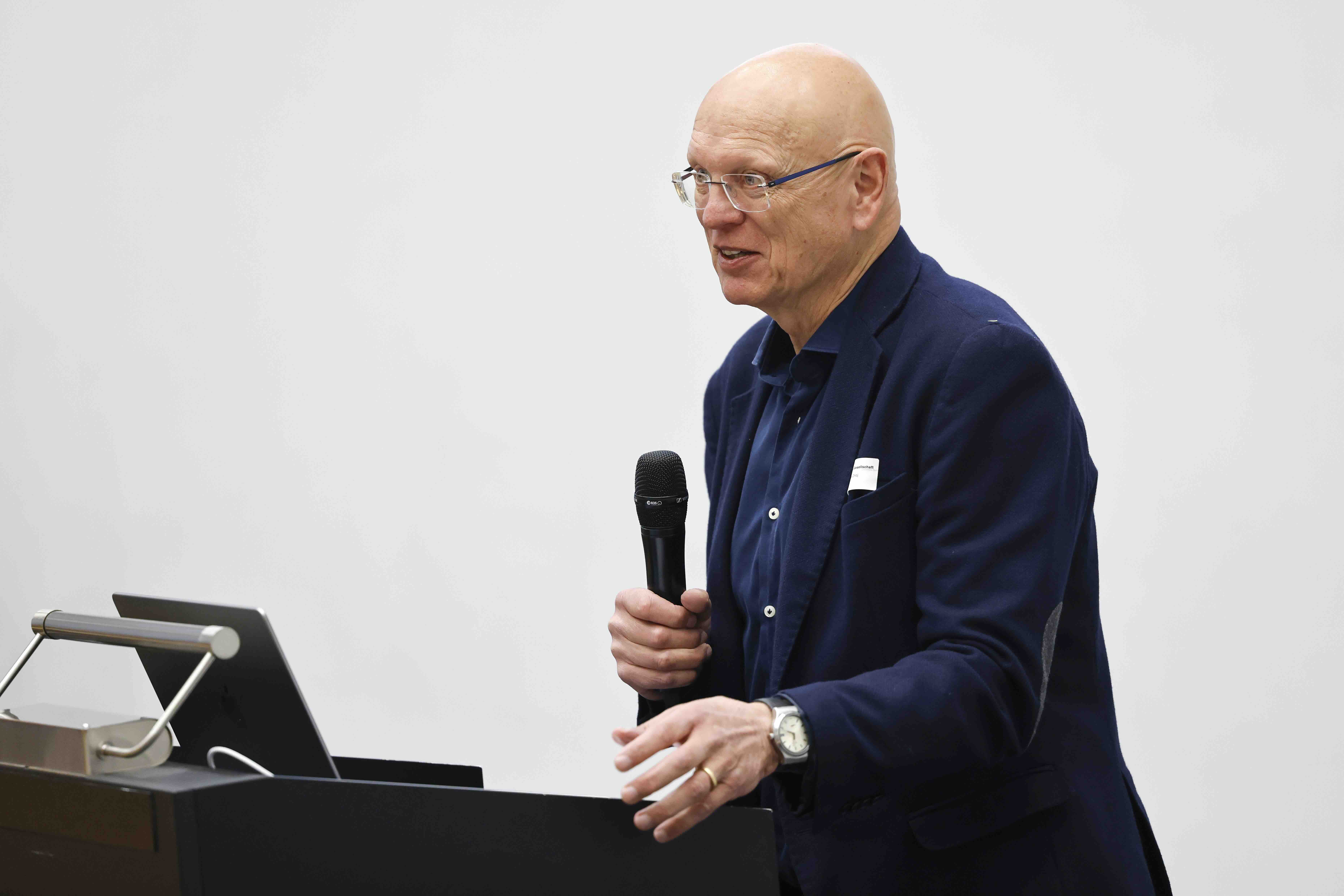 Ein Mann mit Brille steht hinter einem Rednerpult und spricht in ein Handmikrofon.