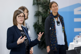 Vier Personen stehen während einer Podiumsdiskussion an zwei Stehtischen mit weissen Tischtüchern. Im Vordergrund ist ein Teil des Publikums sichtbar.